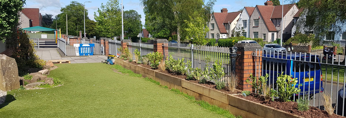 A grassy school playground with wooden planters next to a road