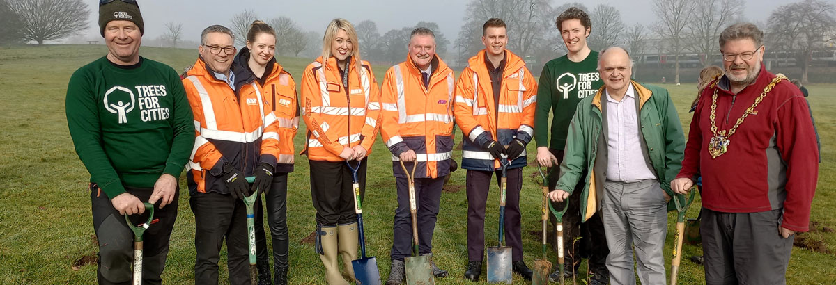People in a line smiling at the camera wearing high-vis & holding shovels